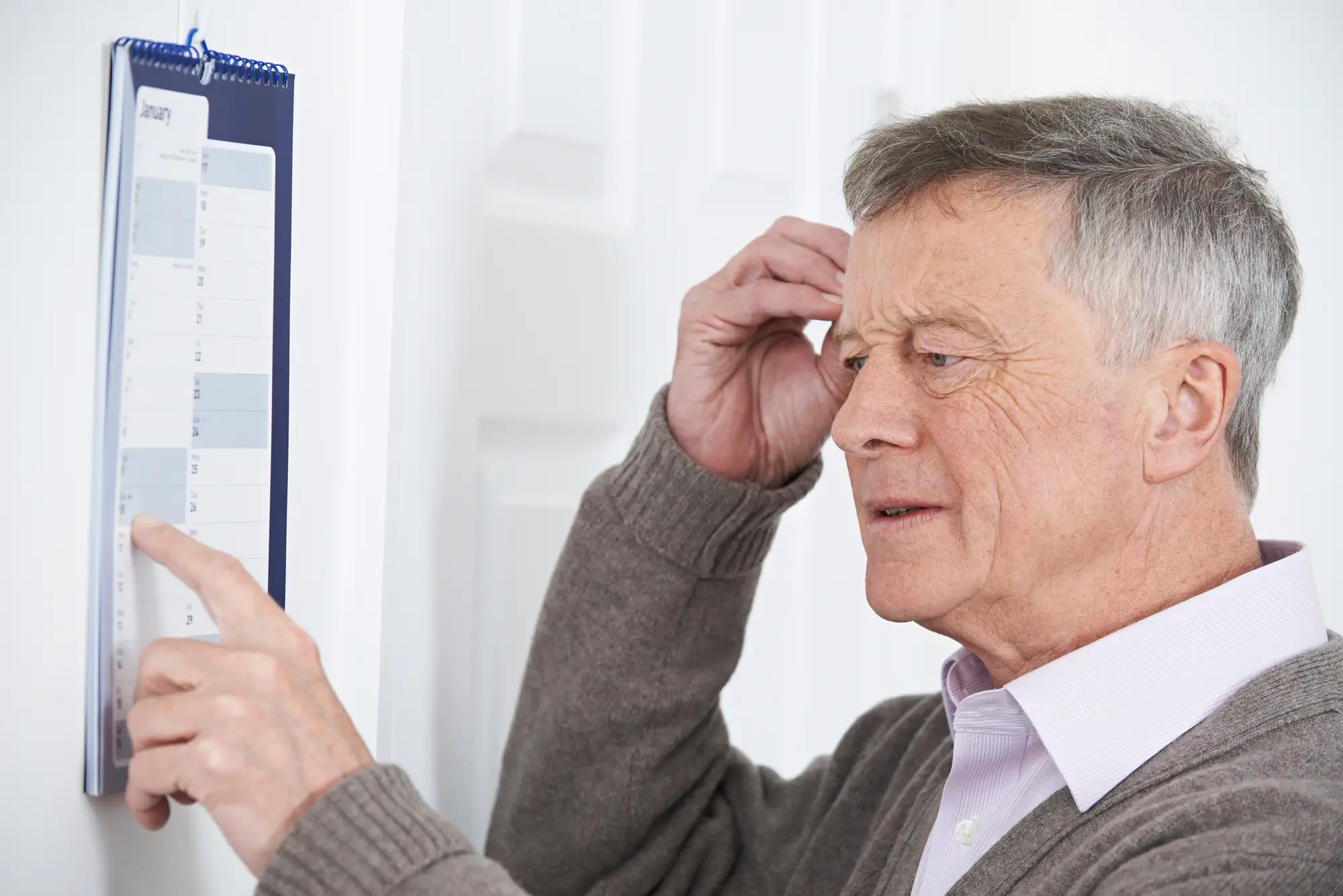senior man with calendar is showing signs of forgetfulness. This shows signs that an elderly parent needs help.